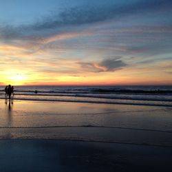 View of calm beach against cloudy sky during sunset