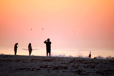 Silhouette people on beach against sky during sunset