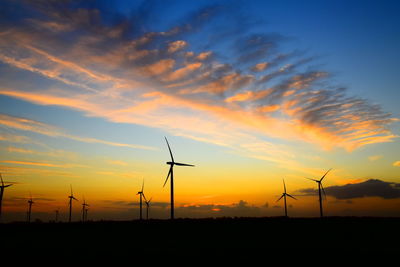 Silhouette wind turbines on land against sky during sunset