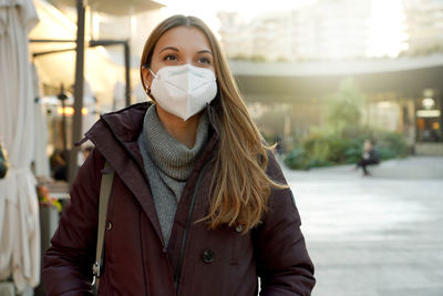 Woman using medical face mask over city background looking to the side and staring away thinking