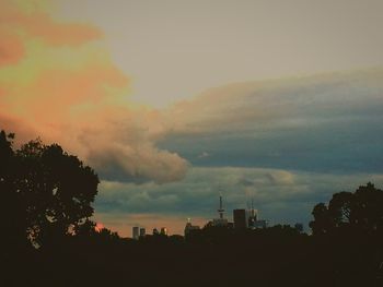 Silhouette of city against cloudy sky during sunset