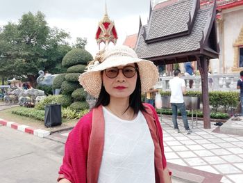 Portrait of woman wearing hat standing against built structure