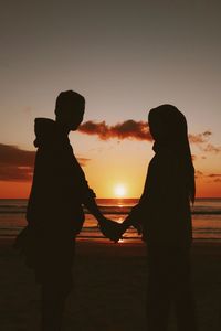 Silhouette couple standing by sea against sky during sunset