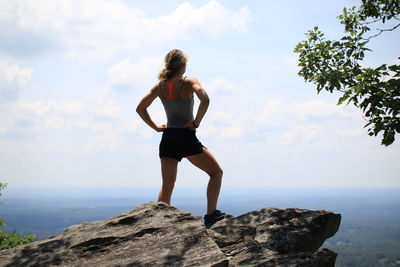 Full length of woman standing on mountain rock by clouds against sky