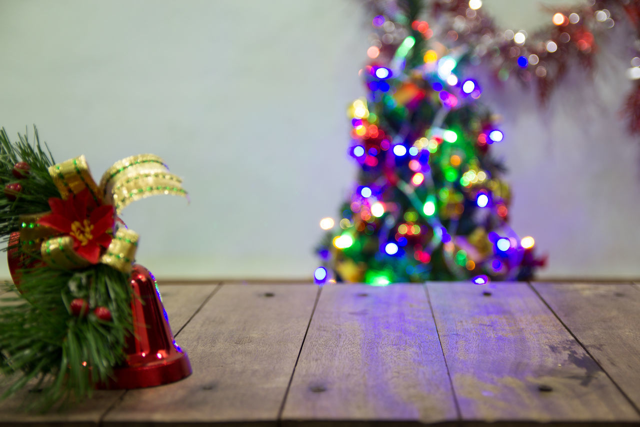 MULTI COLORED CHRISTMAS TREE ON TABLE AGAINST ILLUMINATED TREES