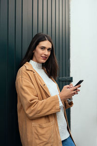 Young woman using mobile phone while standing on wall