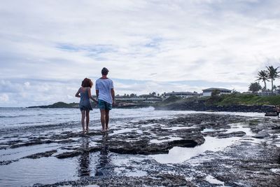 Rear view of couple walking on shore against sky
