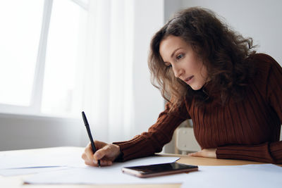 Side view of woman using mobile phone while sitting on table