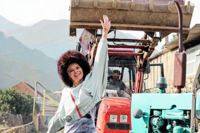 Portrait of smiling young woman with arm raised standing against earth mover