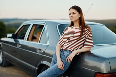 Portrait of young woman sitting on car