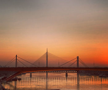 Bridge over calm river against orange sky