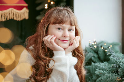 Happy young girl sitting by the window and christmas tree