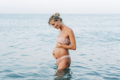 A beautiful pregnant woman stands in the sea and holds her belly. the concept of  motherhood.