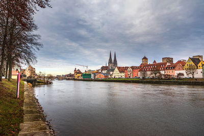 View of buildings by river against cloudy sky