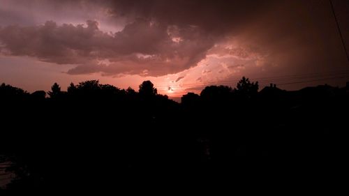 Silhouette trees against dramatic sky during sunset