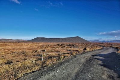 Dirt road on field against sky