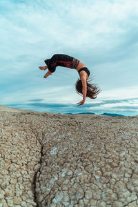 Full body of barefoot female balancing on handstand while practicing yoga pose in dried soil terrain