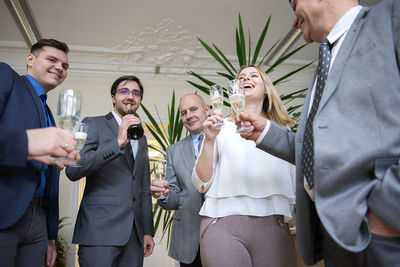 Successful business people are clinking glasses of champagne and smiling while celebrating in office