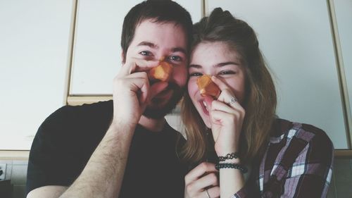 Portrait of happy couple holding food over nose at home