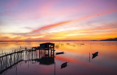 Silhouette wooden posts in lake against sky during sunset