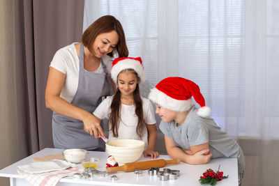 Mom and two children in red caps cooking christmas cookies in the kitchen.