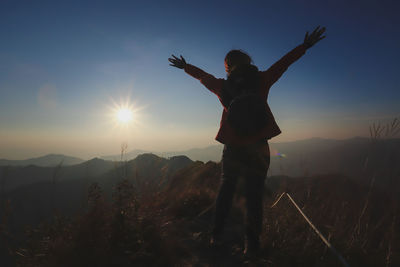 Rear view of silhouette woman with arms raised standing on mountain during sunset