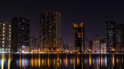 Illuminated buildings by river against sky at night