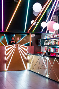 Concentrated young bearded male dj in headphones standing at illuminated counter in modern nightclub