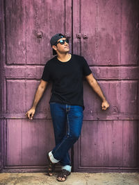 Portrait of man wearing sunglasses standing against door