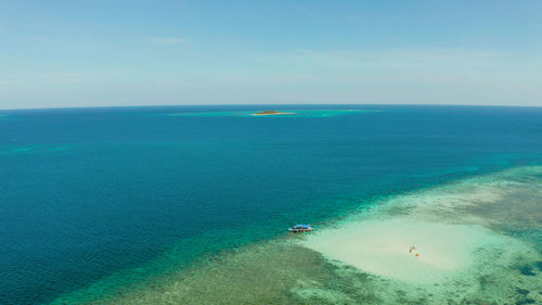 Sandy beach with tourists on a coral atoll in turquoise water, from above.  balabac