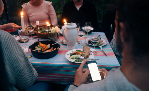 Cropped image of young man using smart phone while having dinner with friends