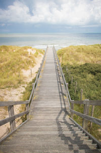 Boardwalk leading towards sea against sky