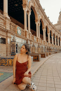 Portrait of young woman sitting in front of historic building