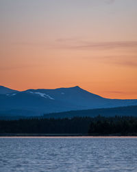 Scenic view of lake by mountains against sky during sunset