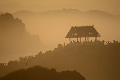 Silhouette building by mountains against sky during sunset