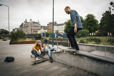 Friends photographing through smart phone while male skater with skateboard on retaining wall