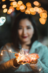 Portrait of woman holding illuminated string lights at night