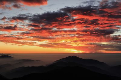 Scenic view of dramatic sky over silhouette landscape during sunset