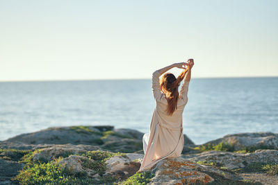 Woman standing on rock by sea against clear sky