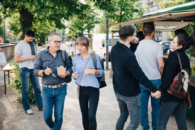 Male and female customer with box talking while couple holding hands and standing by food truck