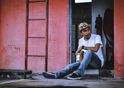 Young man looking away while sitting on doorway