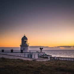 Lighthouse by sea against sky during sunset