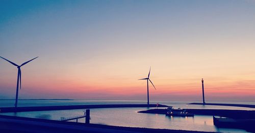 Scenic view of windmills at sea against a clear sky during sunset