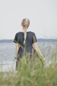 Woman with braided hair from behind standing on beach against sky