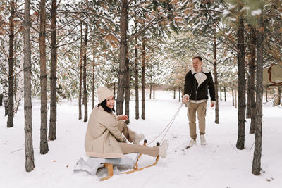 A man and a woman in love have fun and ride sleigh in the forest among the trees in winter in nature