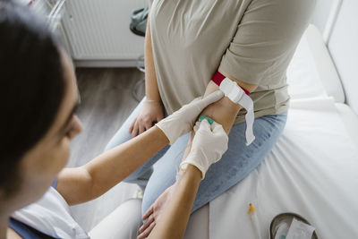 Doctor wearing glove piercing needle in patient's arm at clinic