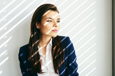 Shadow of blinds on thoughtful woman looking away against wall