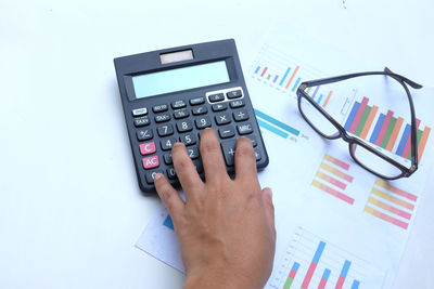 Cropped hand analyzing chart with calculator on desk