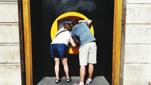 Rear view of man and woman using atm