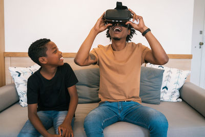 Father using virtual reality goggles while sitting on sofa with son at home